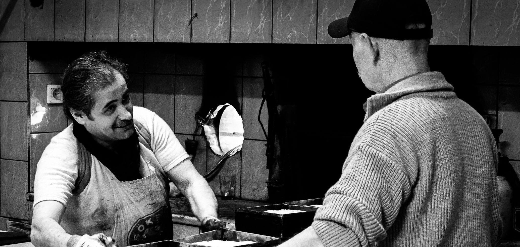 Two bakers prepare bread loaves in a traditional bakery, captured in black and white.